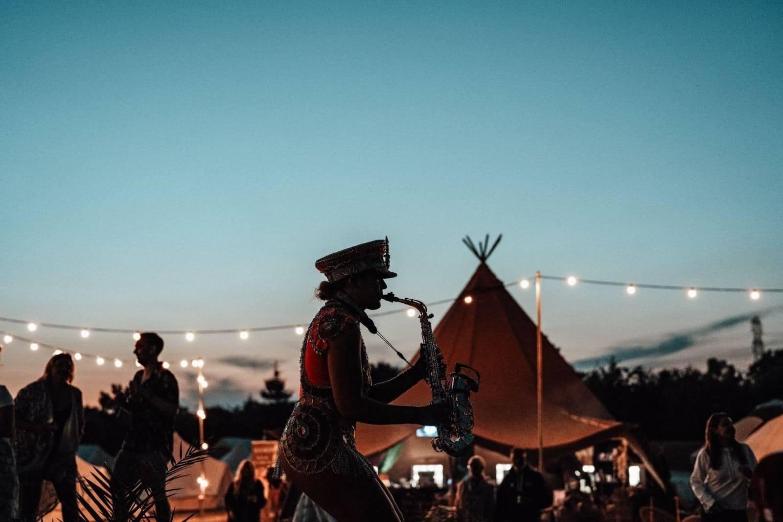 A saxophonist playing at sunset by a tipi